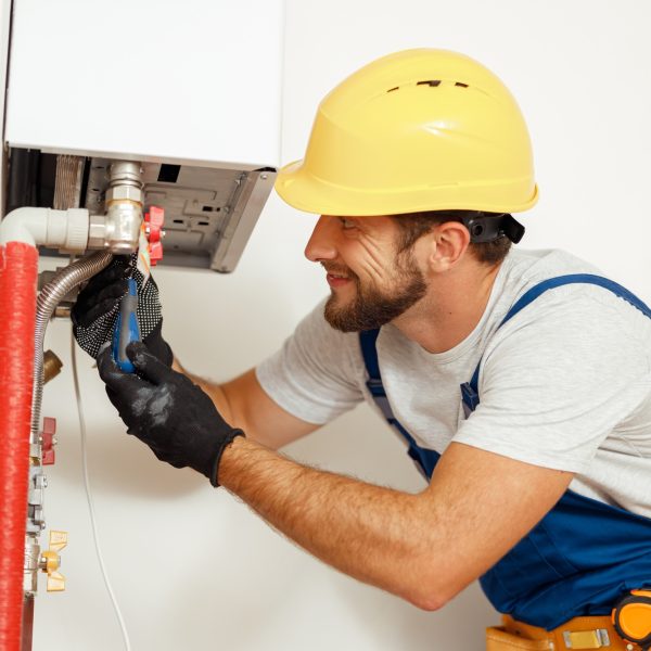 Side view of handyman, technician using screwdriver while fixing boiler or water heater, working on